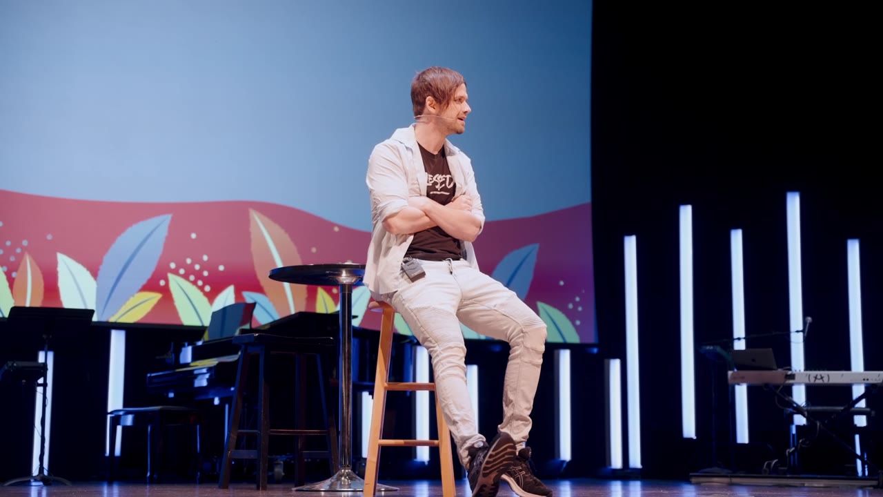 A speaker on a stool on a colorful stage