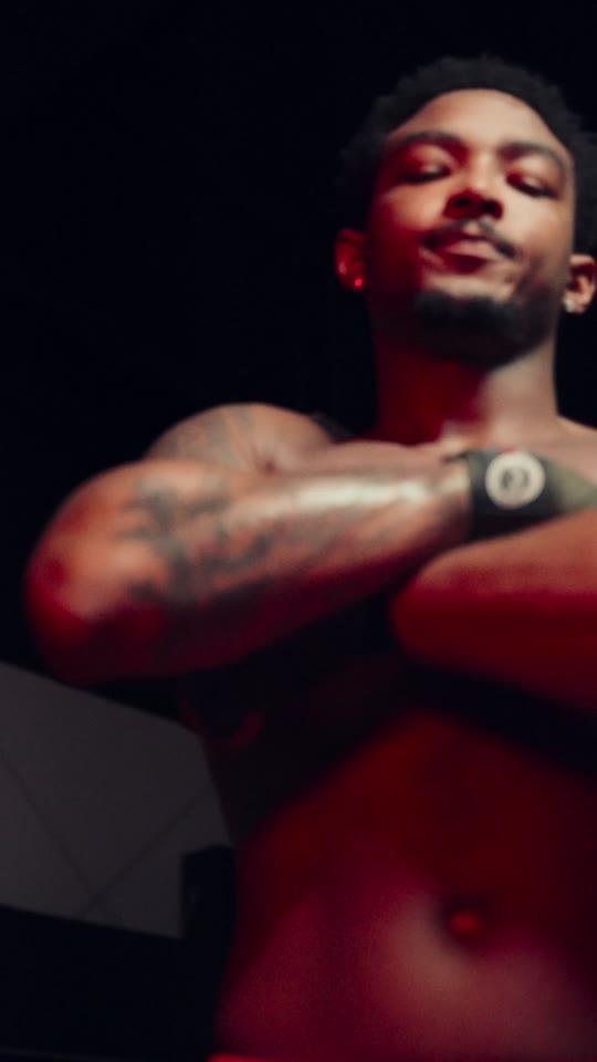 A shirtless fighter with arms crossed under red light