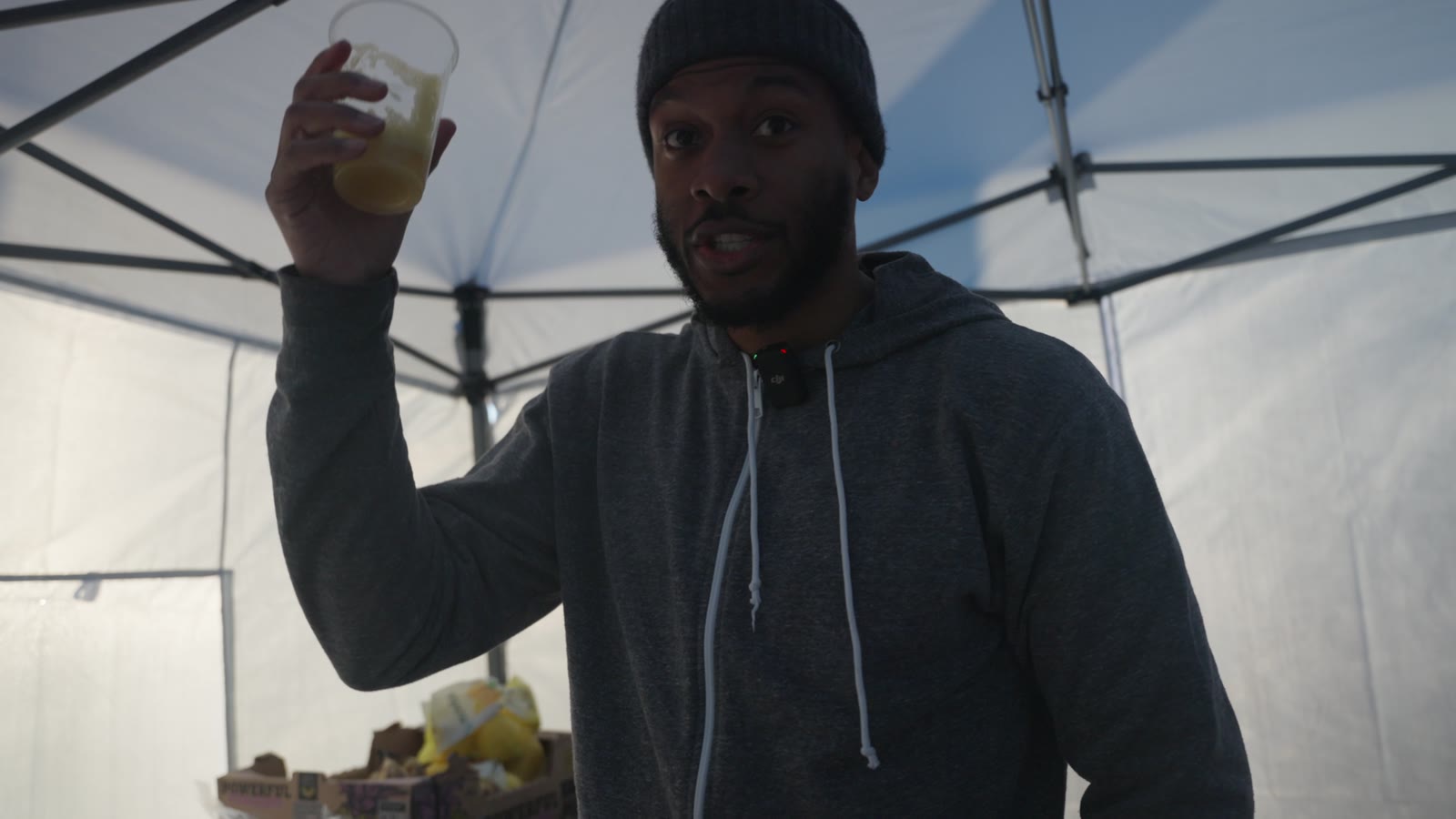 Eli Goree raising a glass of juice in a white tent