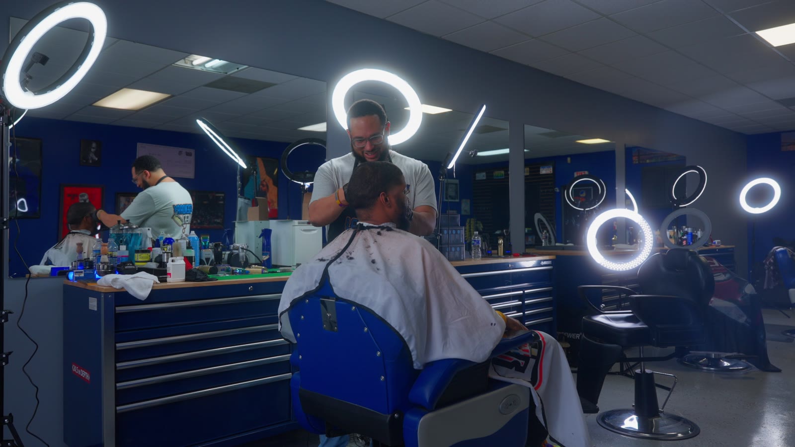 A barber cutting hair in a shop lit by ring lights
