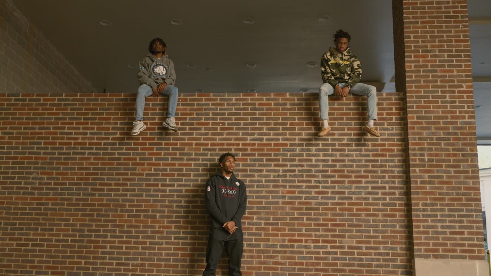 Three young men posed on and against a red brick wall