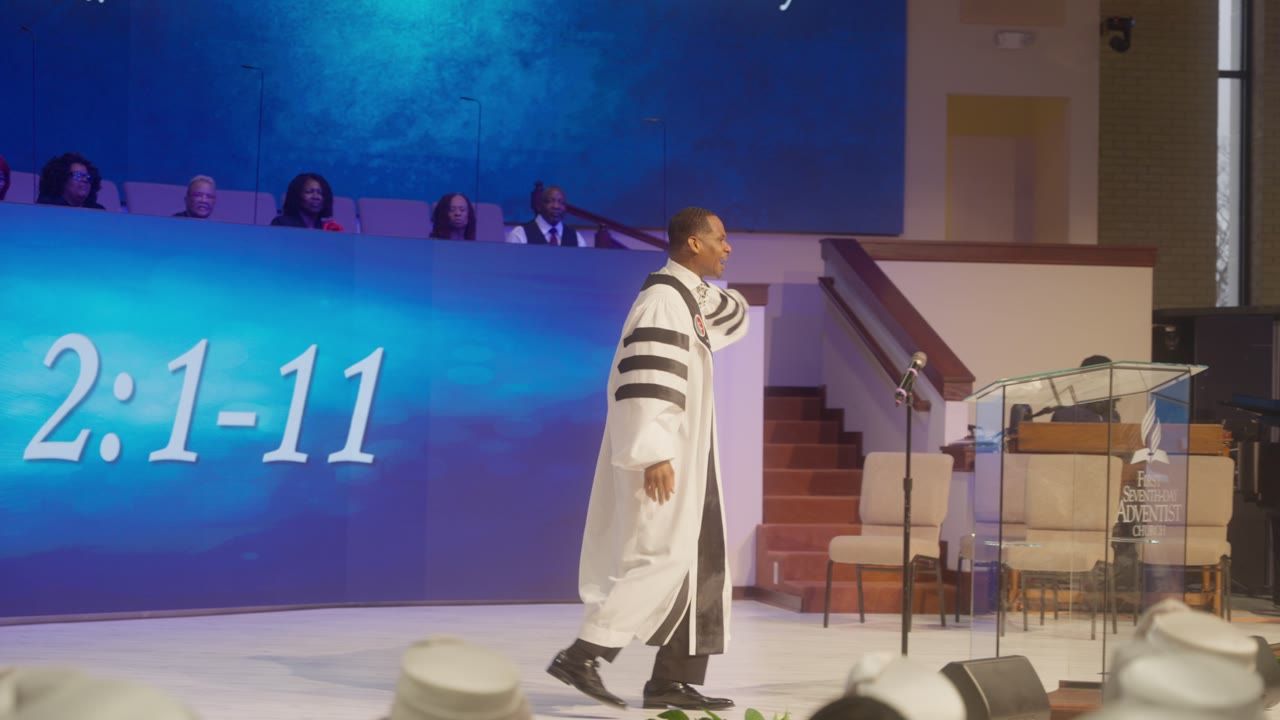 A pastor preaching in front of a blue screen