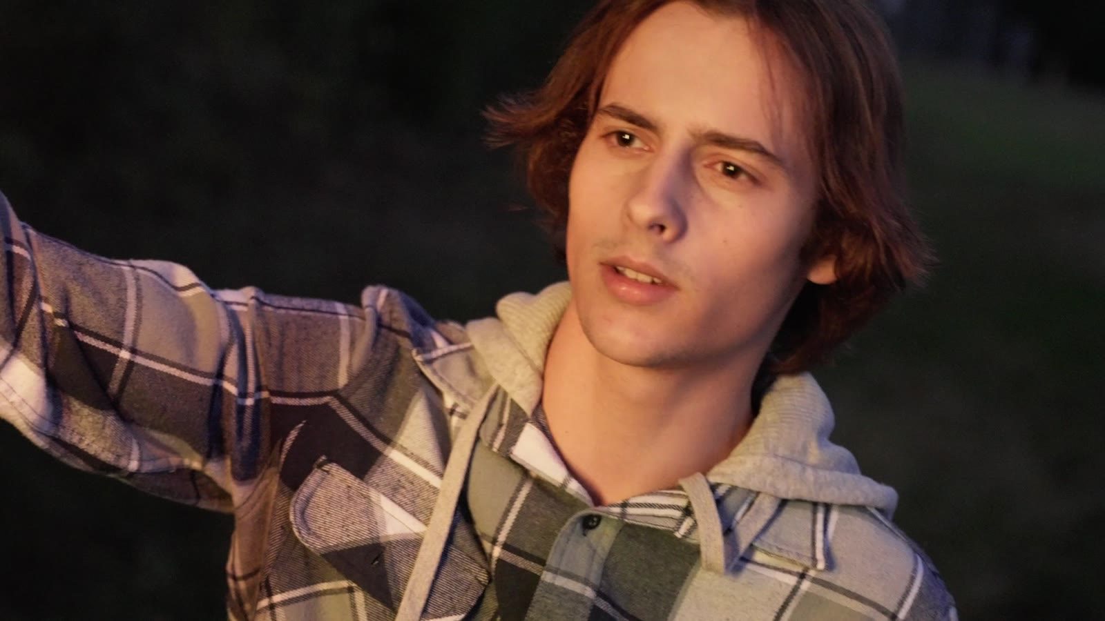 A young man in a flannel reaching out in warm evening light