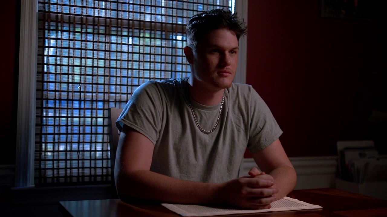 An actor seated at a table in a moody room