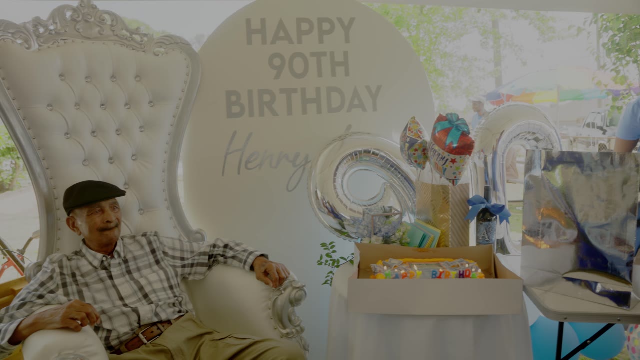 A man seated beside a Happy 90th Birthday display