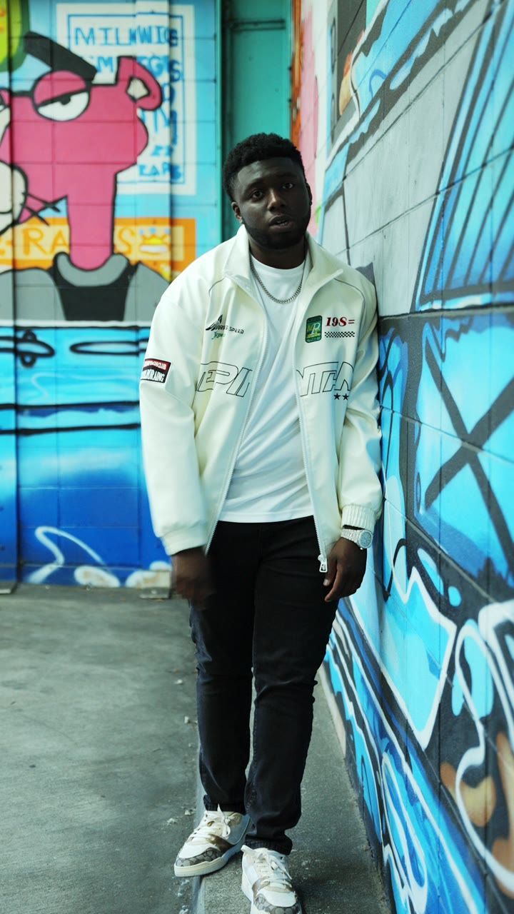 Artist Elisha in a white jacket against a graffiti wall