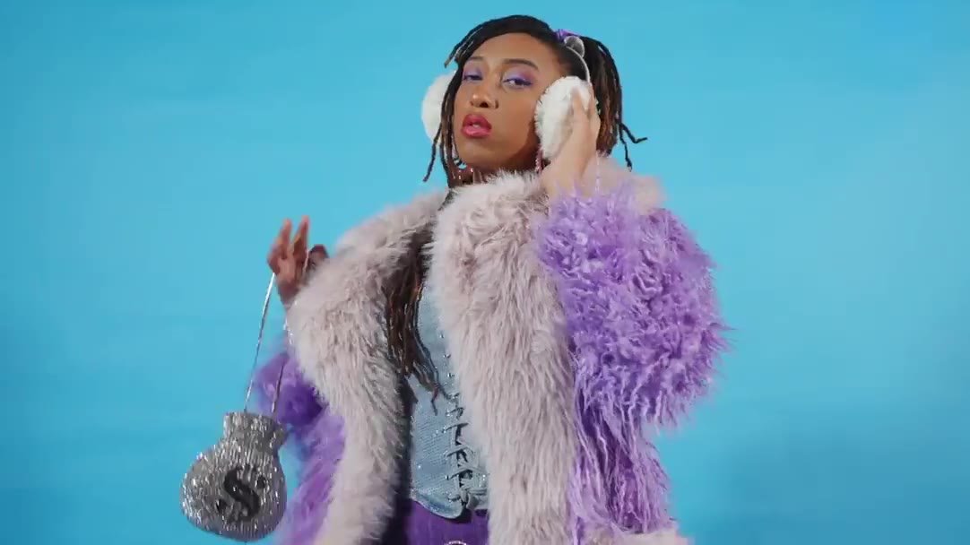 A model in a lilac faux-fur coat and earmuffs on a blue studio backdrop